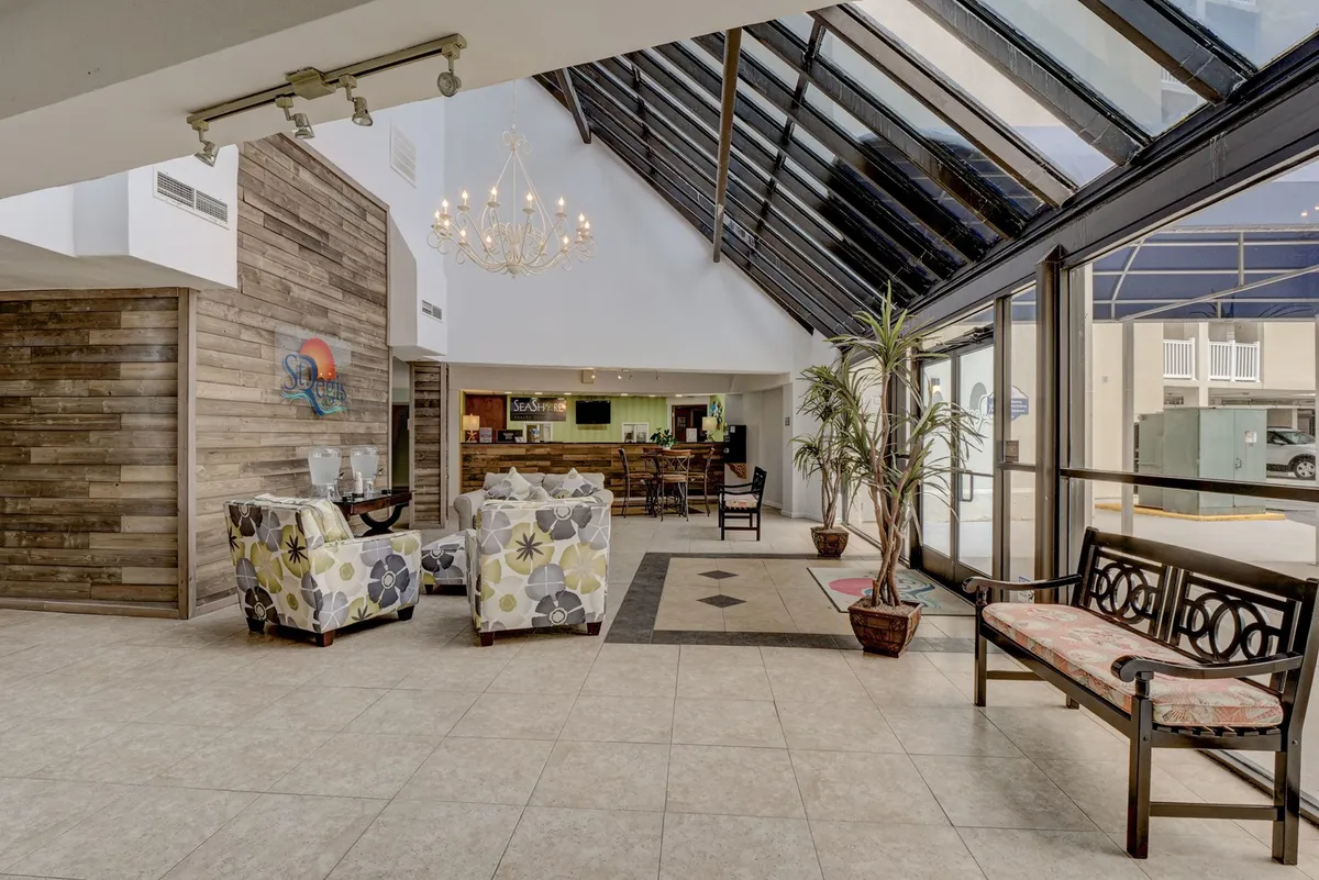 A welcoming interior lounge area featuring a chandelier, comfortable lounge chairs, a reception desk, and indoor plants. It presents a stylish, relaxed environment where guests might gather, socialize, or transition between work and leisure.