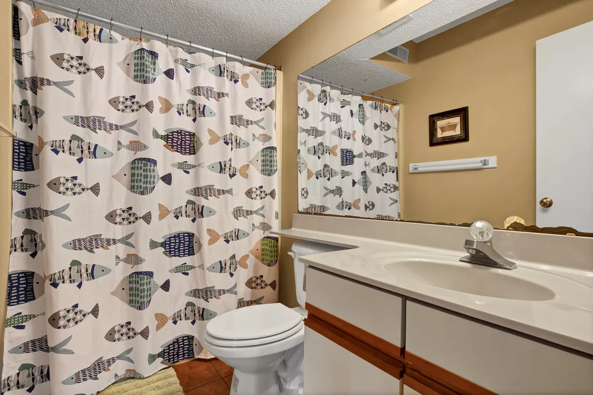 A cheerful bathroom with a playful fish-patterned shower curtain, a vanity mirror, and a tidy sink area. The space feels bright, clean, and welcoming—perfect for both kids and adults.
