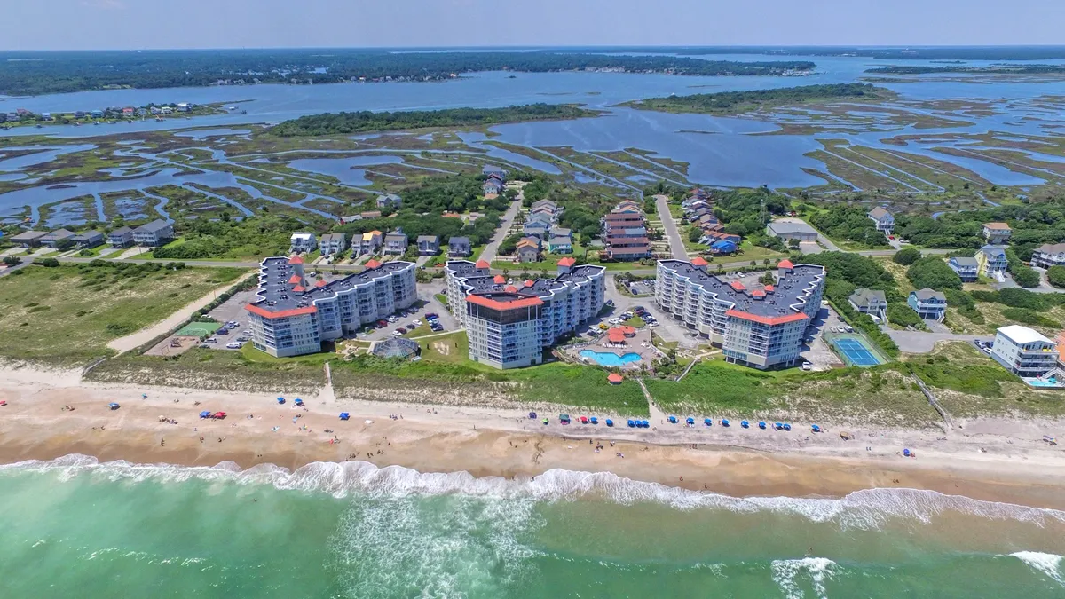 A vibrant exterior image displaying the resort’s coastal buildings, a beachfront area, a glistening swimming pool, and the rolling waves of the ocean beyond. The scene captures the expansive setting, inviting pool, and direct access to the beach—ideal for tranquil walks or lounging by the water.