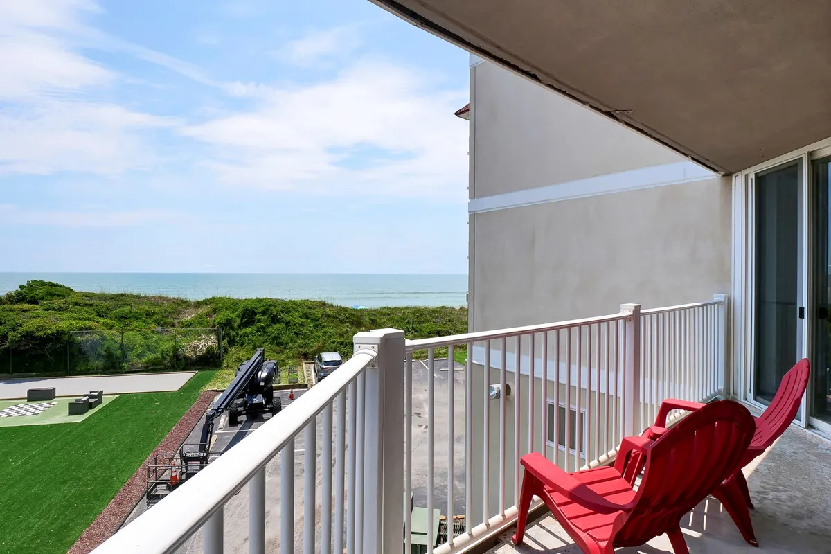 A serene outdoor scene featuring two red chairs on a green lawn, positioned to take in a breathtaking, unobstructed view of the ocean. The setting suggests a private and tranquil spot ideal for couples to relax, enjoy the view, or share a morning coffee or sunset cocktail together.