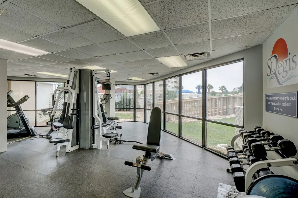 A well-equipped fitness center with modern exercise machines, free weights, and large windows letting in natural light. The layout encourages both individual workouts and group activities, aligning with active wellness.
