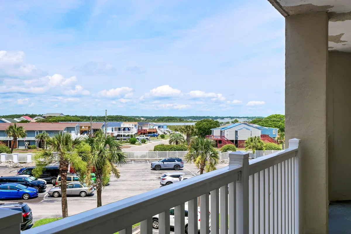A balcony scene showcasing a tranquil water view framed by palm trees and the roofs of neighboring houses, inviting the viewer to imagine stepping outside for a breath of fresh air or a quick break from work. The peaceful setting hints at the soothing presence of the ocean and the opportunity to enjoy the outdoors right from the condo.