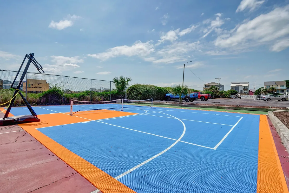 A vibrant, colorful outdoor sports court featuring a basketball hoop and tennis net, surrounded by greenery. The lively design and multi-functional nature of the space highlight opportunities for active group recreation and friendly competition.