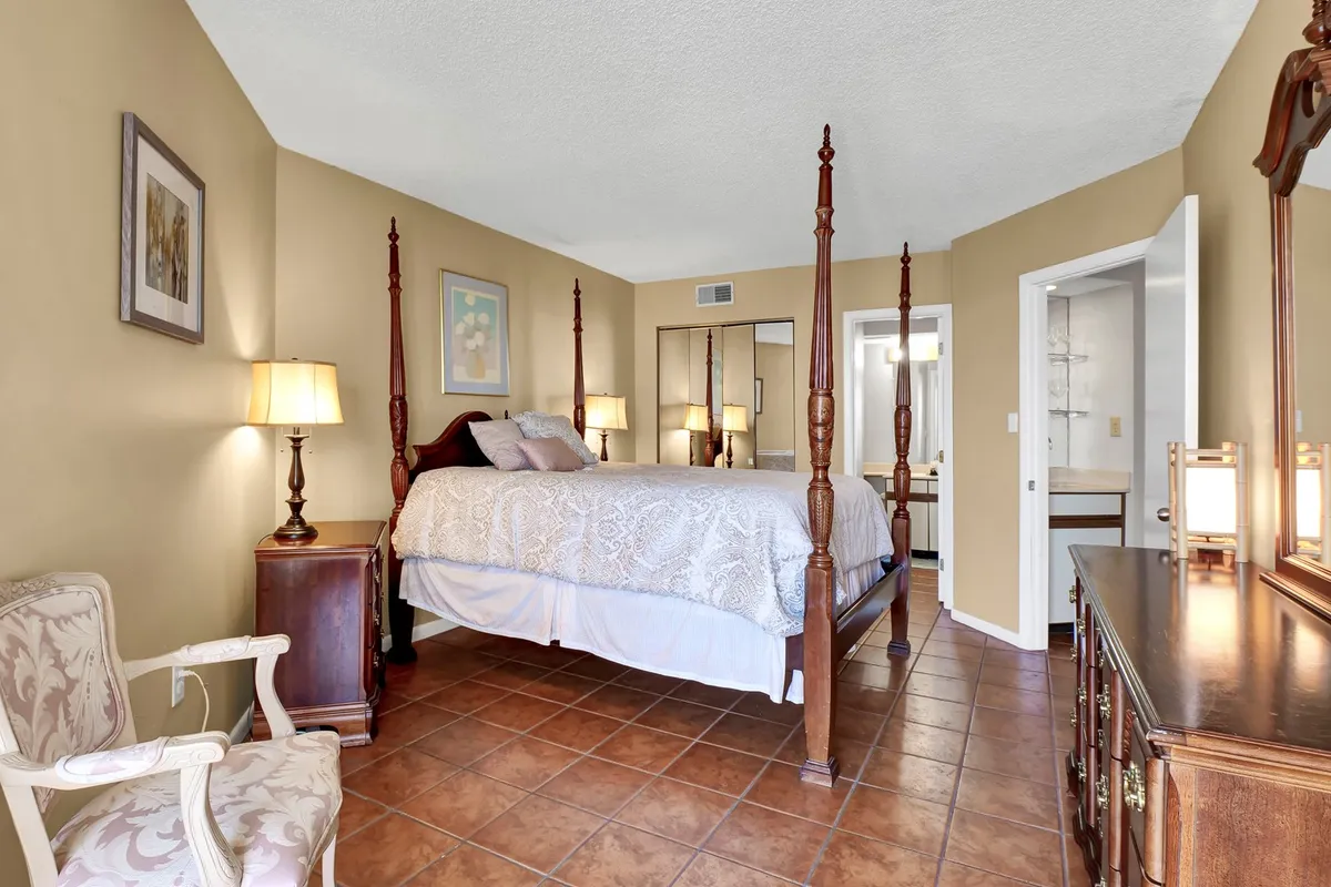 A tranquil bedroom featuring a four-poster bed, decorative chair, and a dressing table situated near a window. Soft natural light filters in, creating a serene, restful atmosphere ideal for relaxation and rejuvenation.