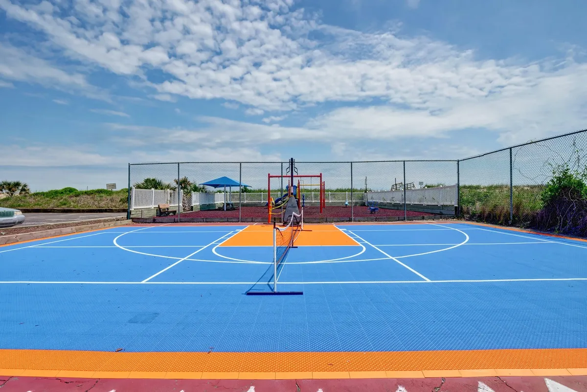 An energetic exterior shot of a colorful sports court surrounded by lush greenery. The court is set up for basketball and tennis, creating a sense of active recreation and community engagement in the resort's outdoor amenities.