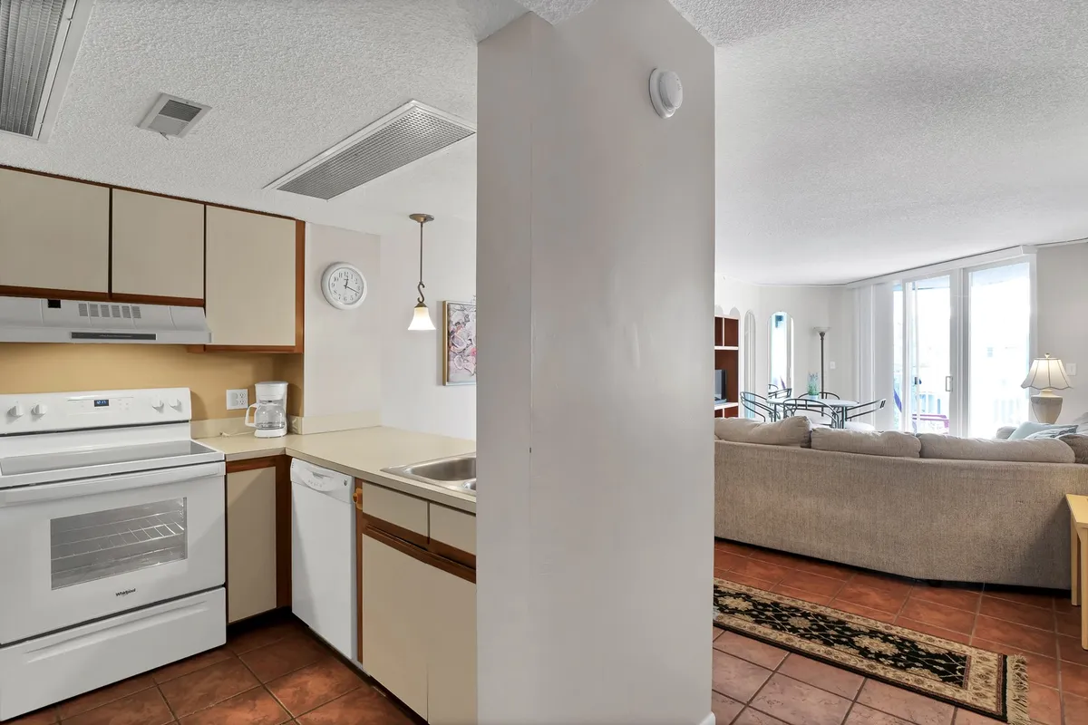 The photo presents an open-plan kitchen and dining area, featuring kitchen appliances, a clean sink, cozy living room seating, and a visible dining table. The space feels warm and inviting, blending cooking, dining, and entertaining in one connected zone.