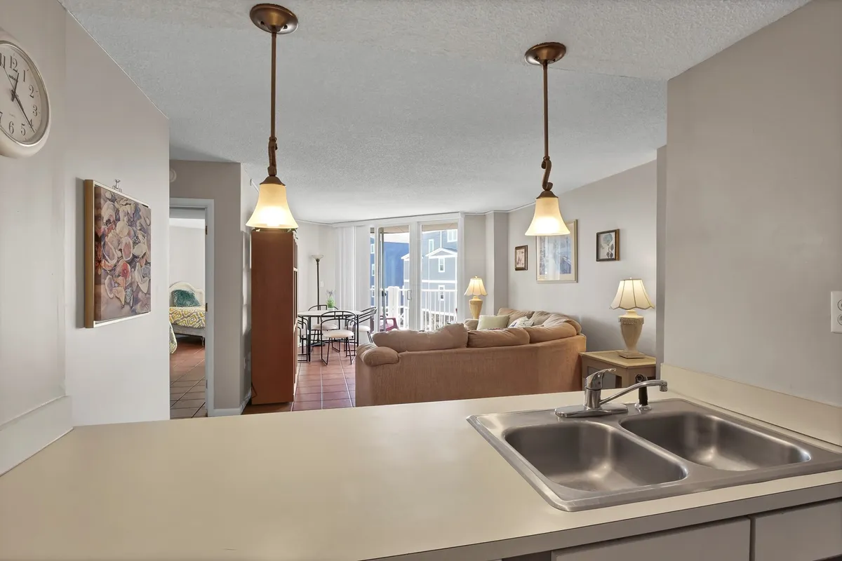 A spacious kitchen with a central island and hanging light fixtures sits adjacent to a large dining table and comfortable living room seating. The setting is inviting and perfect for hosting group meals or casual celebrations, with plenty of room for both cooking and dining.