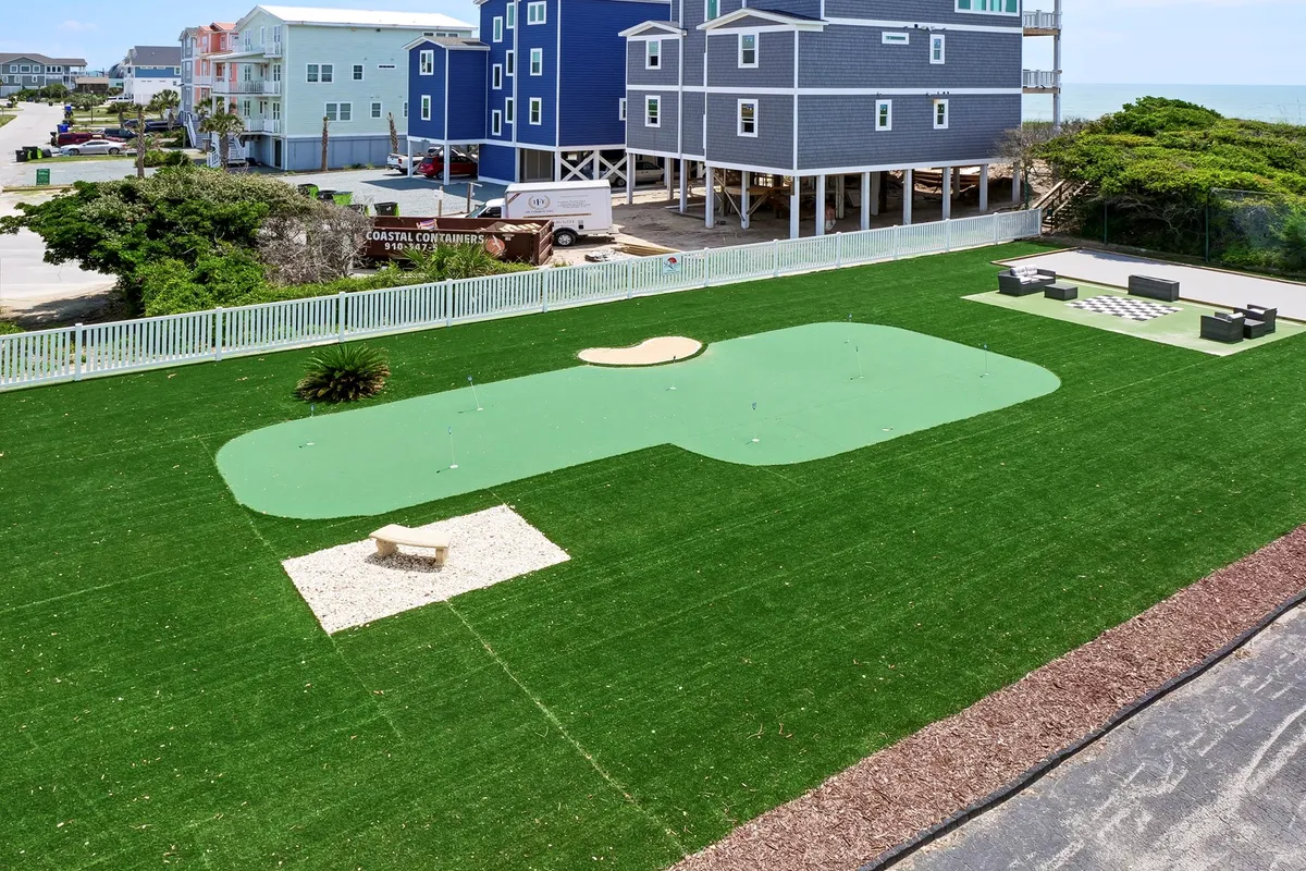 An exterior scene showing a putting green, outdoor seating area, and a lush green lawn. The space feels open and relaxed, offering options for golf practice, picnics, and casual socializing in the fresh air.
